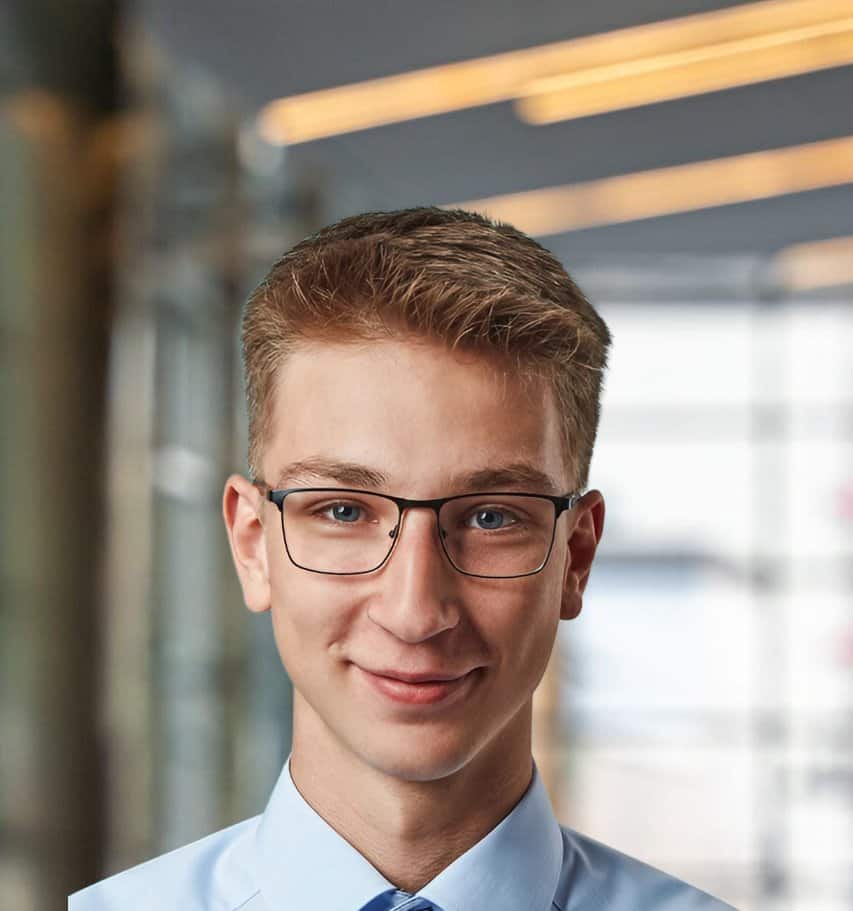 Young man in business attire with glasses smiling at the camera.